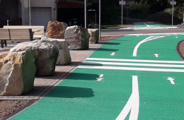 Foto von einem neuen Radweg. Der im Bild zu sehende Abschnitt ist grün und die Fahrtrichtung ist mit Pfeilen gekennzeichnet. Am Wegrand stehen große Steine.