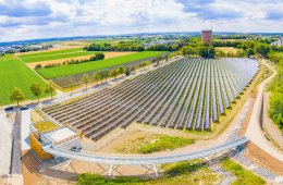 Ein Steg führt auf ein Technikgebäude, von dem aus man über ein Solarfeld blickt