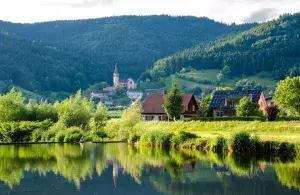 Das Bild zeigt ein Dorf in einer ländlichen Umgebung mit Bergen und einem See. 