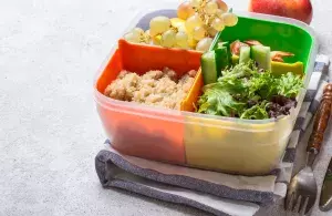 Das Bild zeigt eine gefüllte Essensbox mit Salat, Weintrauben und anderen Beilagen.