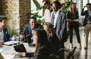 Menschen im Business-Outfit tauschen sich bei einem Vernetzungstreffen an einem großen Tisch und im Raum aus.