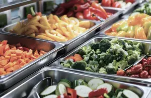 Frisches, buntes Gemüse wie Brokkoli, Paprika und Tomaten in Edelstahlbehältern an einer Mensa-Salatbar.