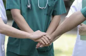 Mehrere Menschen in medizinischer Kleidung legen im Freien ihre Hände übereinander als Zeichen für Teamgeist.