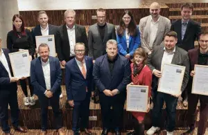 Eine Gruppe von Menschen steht auf einer Treppe und hält Urkunden für ihr klimafreundliches Unternehmensengagement.