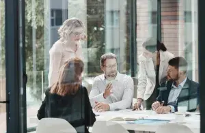 Mehrere Personen besprechen sich an einem Konferenztisch in einem hellen Büro mit großen Glasflächen.