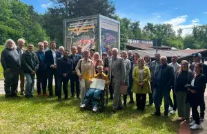 Eine Gruppe steht im Freien vor einem Gebäude, in der Mitte hält eine Person eine Urkunde.