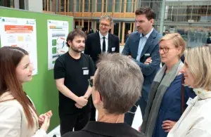 Mehrere Personen stehen in einem modernen Foyer vor einer Stellwand mit Projektpostern und tauschen sich aus.