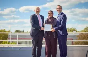 Drei Personen stehen vor Solarmodulen der Universität Bonn und halten gemeinsam den Förderbescheid in die Kamera.