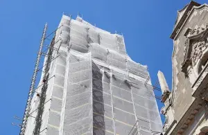 Von Gerüst und Schutznetz umhülltes hohes Gebäude vor blauem Himmel