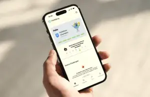 Eine Hand hält ein Smartphone mit der geöffneten Fit4Klima-App, die Punkte in einer Aufgabe und Erfolgsbalken anzeigt.