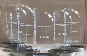 Sechs Trophäen aus Glas stehen auf einem Holztisch, darauf stehen die Namen der Gewinnenden, sowie das Logo des Projekts „Klimaretter-Lebensretter“ und der Text „Klimaretter-Award“.