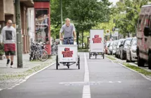 Das Bild zeigt zwei Lastenrad fahrende Personen auf einem breiten Fahrradweg. 