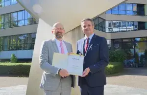 Zwei Männer übergeben vor einem Bürogebäude eine Förderurkunde über rund 1,4 Millionen Euro.