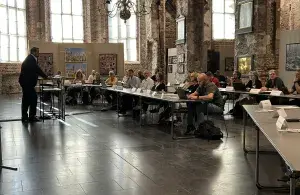 Der Oberbürgermeister steht an einem Redepult, vor ihm sitzen die Teilnehmenden an langen Tischen.
