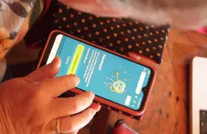 Zu sehen ist, von oben aufgenommen, ein kleiner Ausschnitt des Gesichts und der Hand einer Person, die auf dem Smartphone das Quiz der „Omas for Future” spielt. 