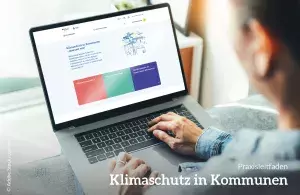 Zu sehen ist eine Person, die einen Laptop auf dem Schoß hat. Auf dem Laptopbildschirm ist die Startseite des digitalen Praxisleitfadens "Klimaschutz in Kommunen" zu sehen.