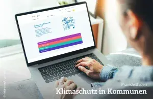 Eine Person, die auf einen Laptop schaut. Auf dem Bildschirm sieht man die Online-Version vom Praxisleitfaden "Klimaschutz in Kommunen"