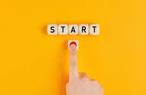 Das Foto zeigt einen Finger, der auf einen roten Punkt drückt. Darüber die Bauklötze mit dem Wort "START" vor gelbem Hintergrund.