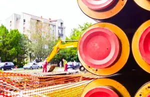 Das Foto zeigt eine Seitenansicht auf rot-orange Rohre, sowie eine Baustelle im Hintergrund