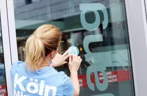 Das Foto zeigt eine Frau von hinten beim Anbringen des Aufklebers „Leitungswasserfreundliches Unternehmen“ an der Firmentür von RheinEnergie in Köln.