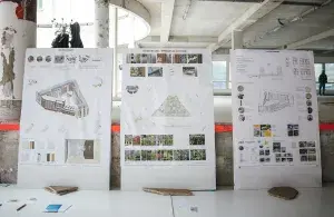 Drei große Architekturpläne stehen in einem Rohbau auf einem Tisch.