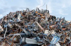 Großer Schrotthaufen aus Altmetall und Industrieabfällen auf einem Recyclingplatz vor hellem Himmel.