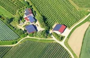 Von oben: landwirtschaftliche Felder mit drei Gebäuden in der Mitte auf denen Photovoltaikanlagen installiert sind